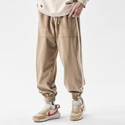 Dark gray relaxed-fit joggers with bold side stripes, snap-button cuffs, and utility front pockets