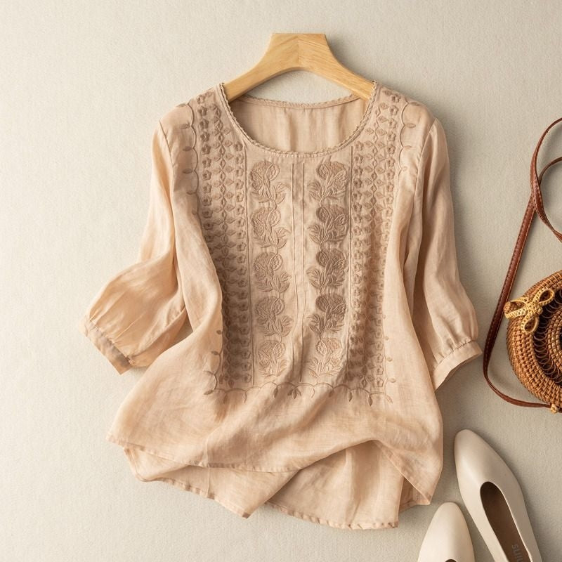 Ivory linen blouse with stitched floral details, subtle gathered sleeves, and curved high-low hem