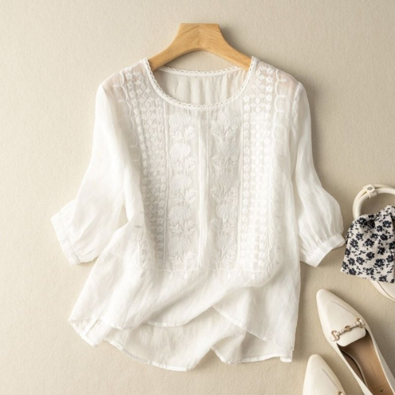 White linen blouse with stitched floral detail, subtle gathered sleeves, and curved high-low hem
