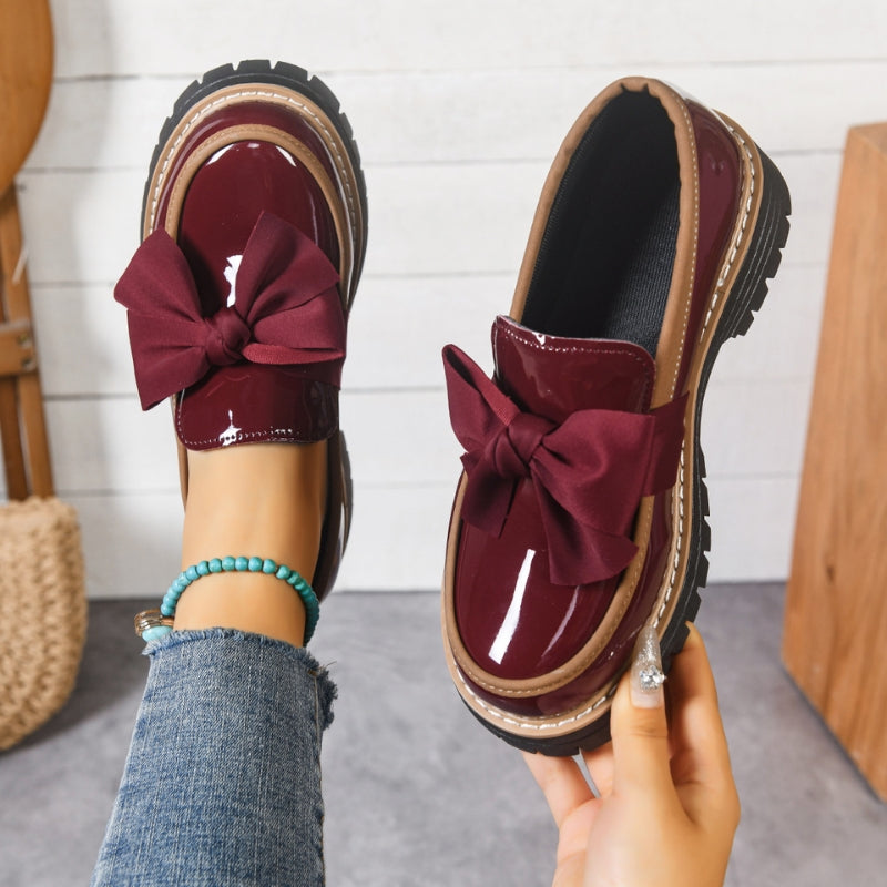 Women's black patent platform loafers with chunky sole and statement bow slip-on detail