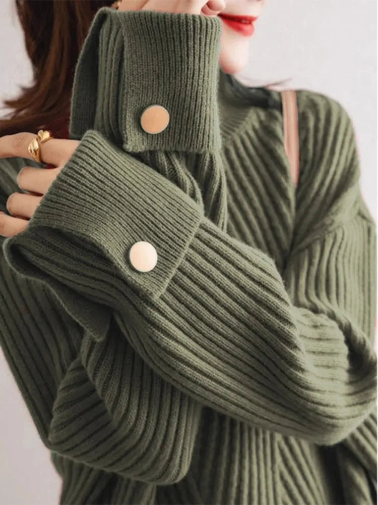 Oversized ribbed knit pullover in neutral tone with high neck, turn-up cuffs, and contrast button detail