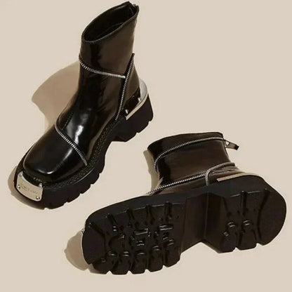 Glossy black patent ankle boots with asymmetric zipper accents, chunky lug sole, and metallic hardware