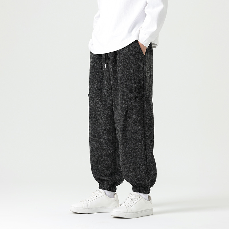 Black minimalist joggers with traditional Eastern knot accents on thigh, tailored drape, elastic cuffs