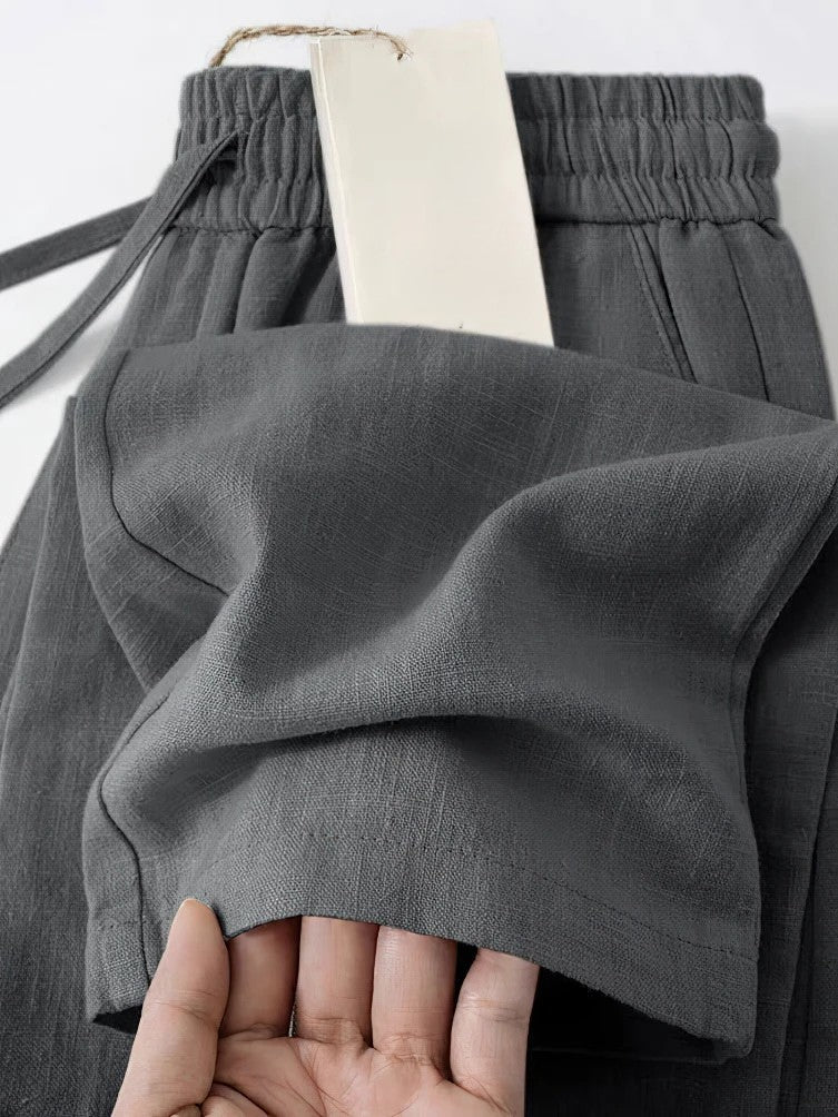 Beige cropped linen pants with pleated details, elastic waist, and relaxed Japanese-inspired silhouette