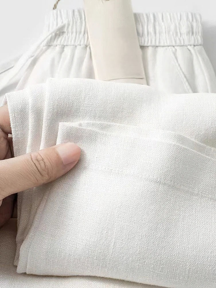 Beige cropped linen pants with pleated details, elastic waist, and relaxed Japanese-inspired silhouette